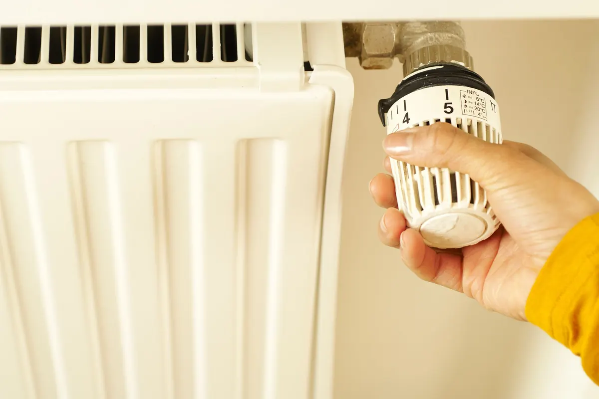 Hand draait aan het thermostaatknopje van een radiator