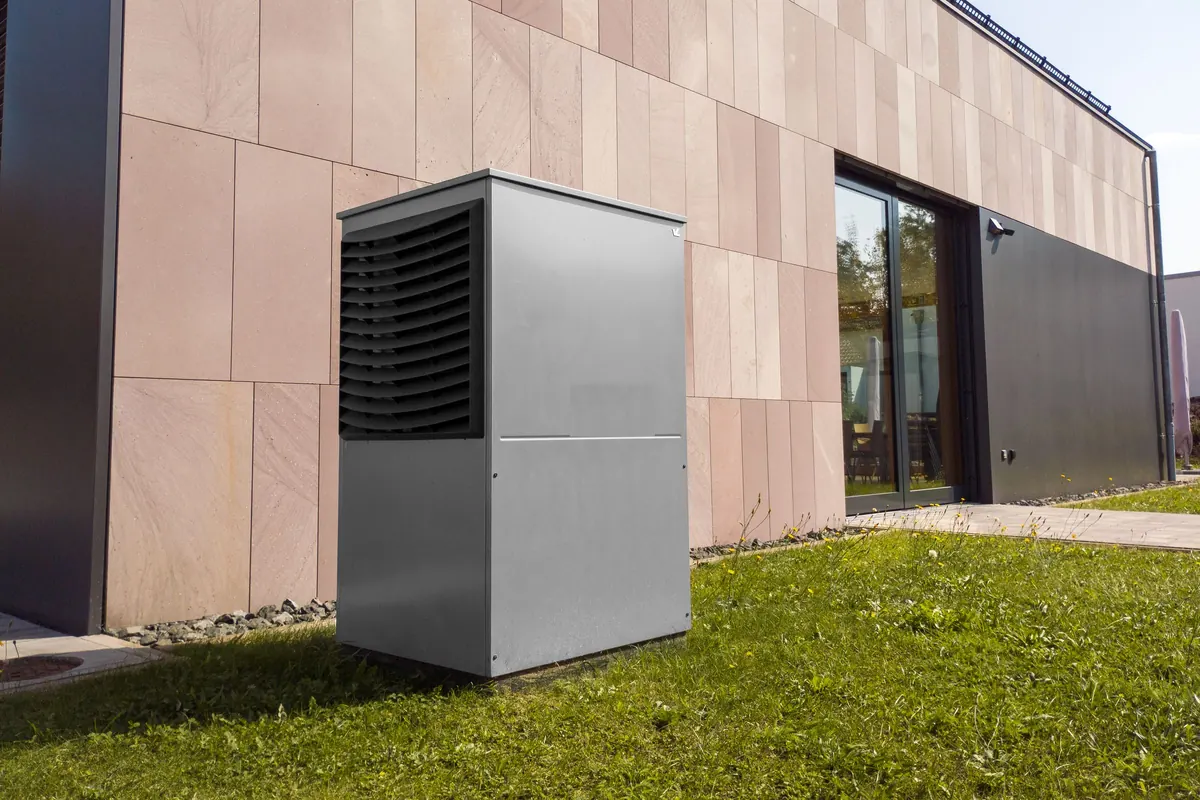Buitenunit van een warmtepomp op het gras naast een woning