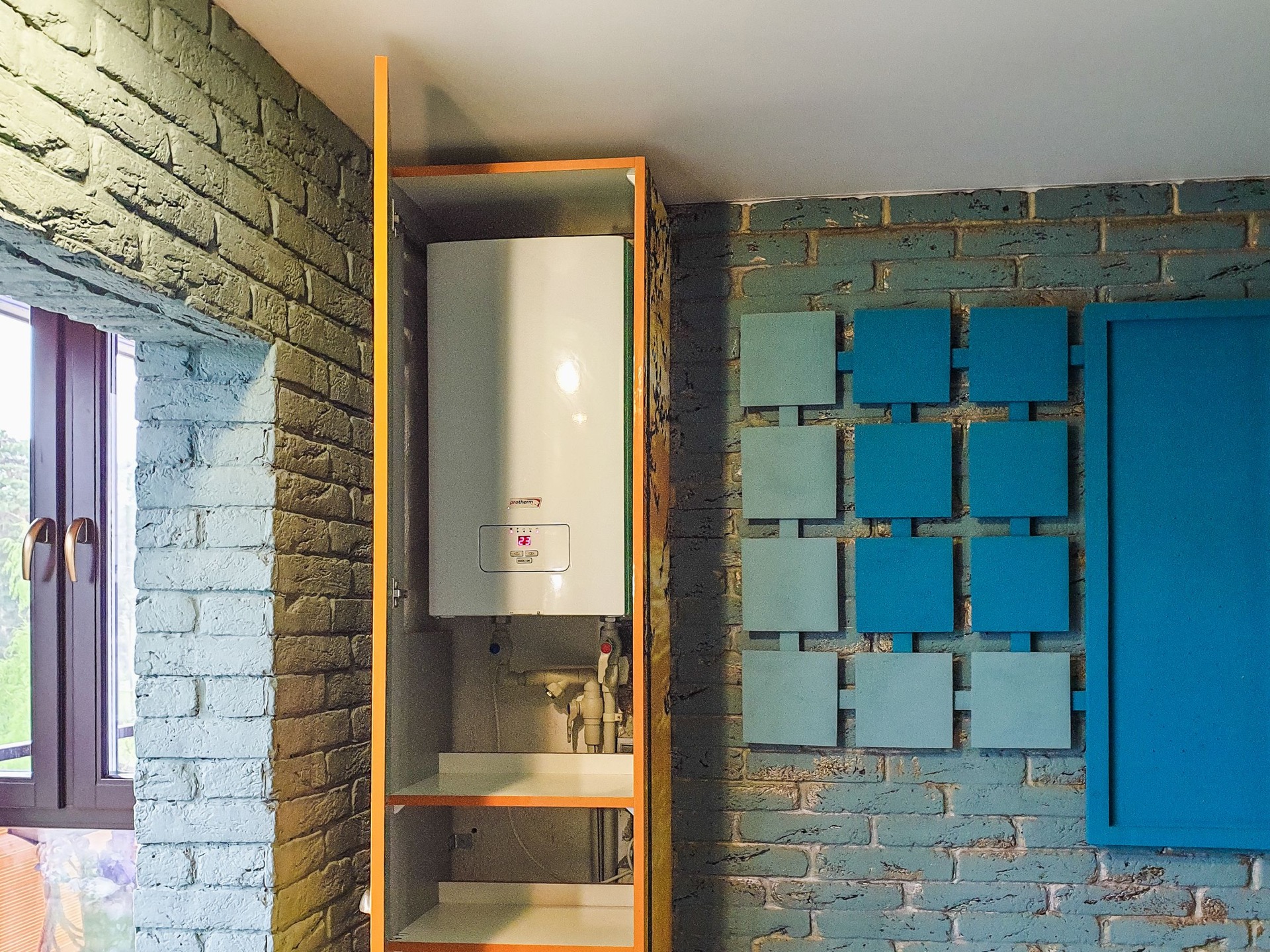 Een witte cv-ketel in een houten nis tussen een blauwe en een groene bakstenen muur
