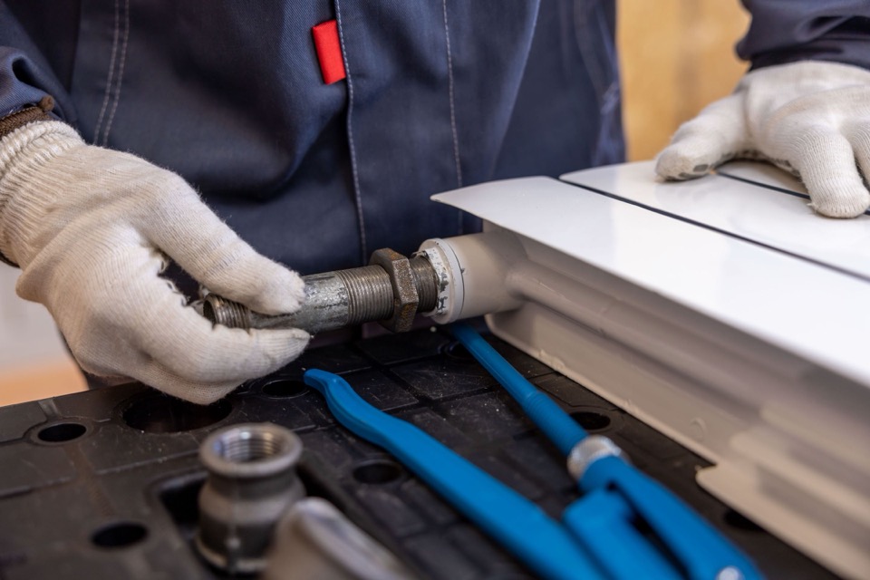 Een monteur zet met handschoenen een leiding vast aan een radiator