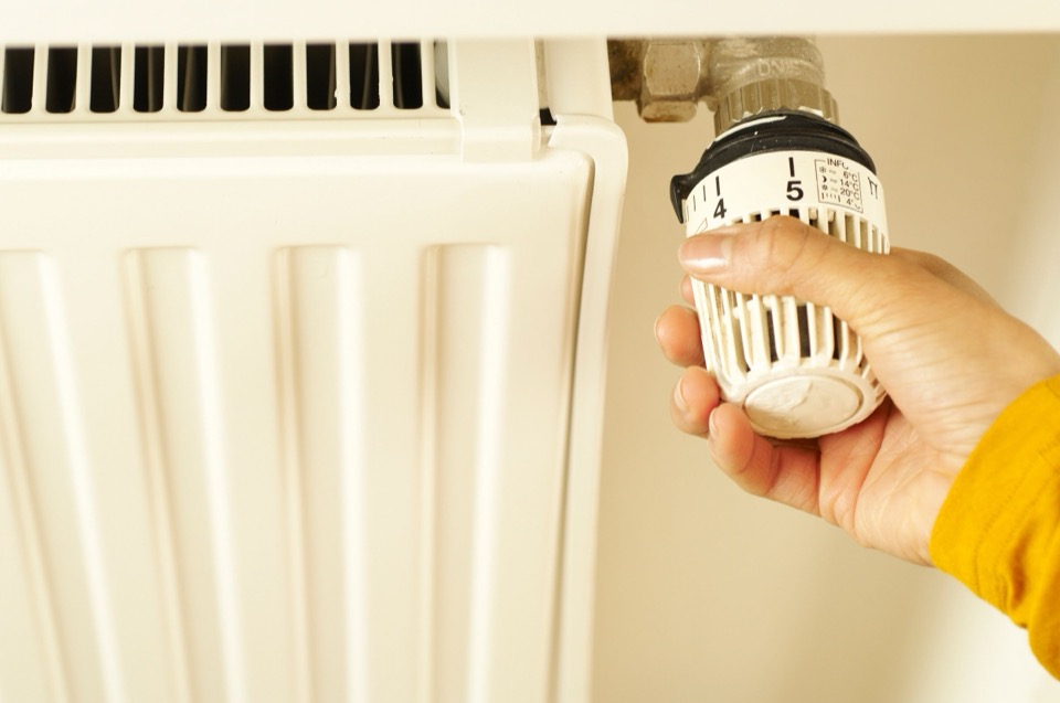 Een hand draait een thermostaatkraan open op een witte radiator