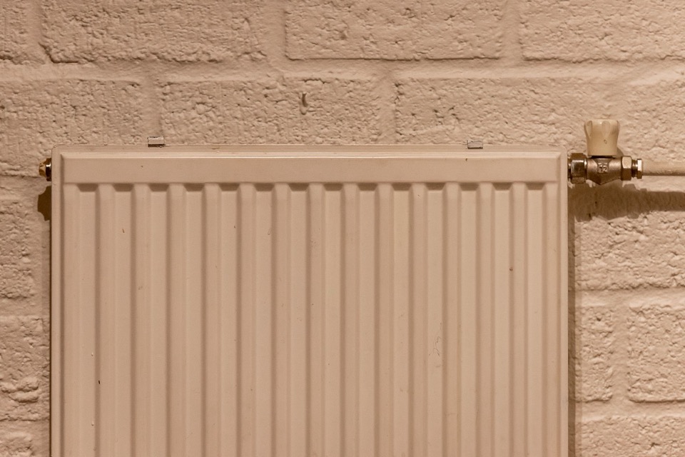 Een wit radiator tegen een muur van geschilderde baksteen met een kraan rechts