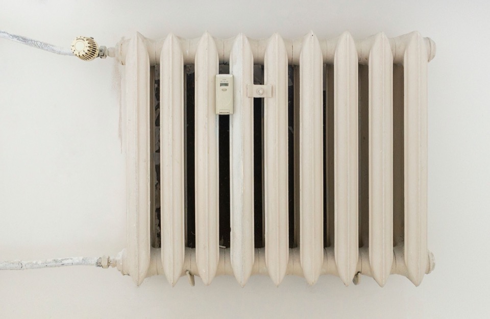 Een witte gietijzeren radiator tegen een lichte muur